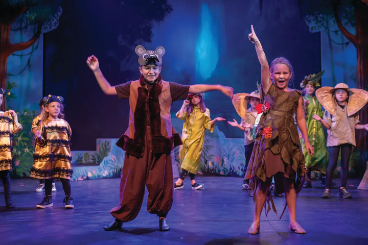A young ensemble in animal costumes on stage in front of a projected jungle