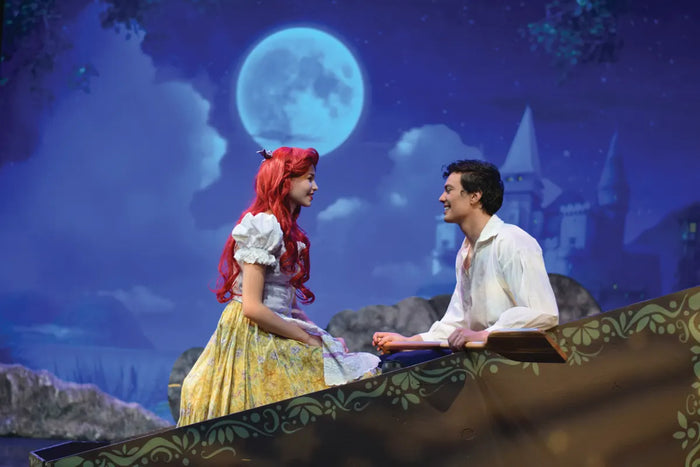 Two performers on a rock beneath a projected moonlit sky