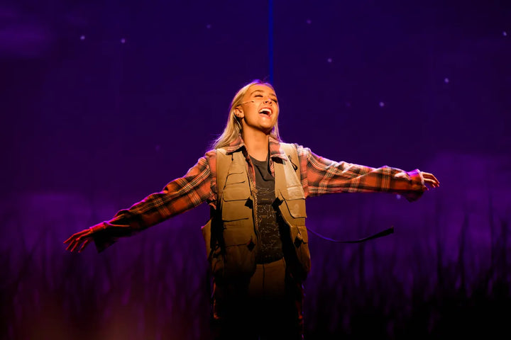 A soloist sings with arms outstretched under purple light